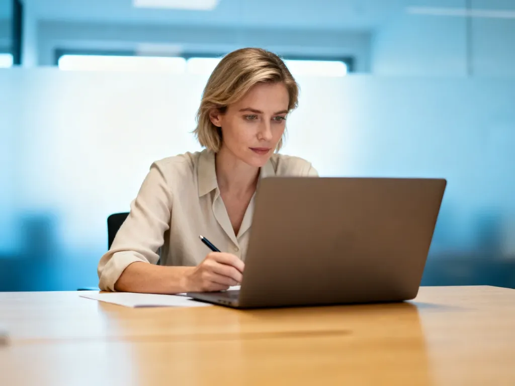 Kobieta pracująca przy laptopie w nowoczesnym biurze, skupiona na obliczeniach finansowych.